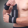 A person is applying black heavy duty wrist wraps to their forearm for strength training.