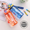 A clear blue dinosaur silicone straw water bottle with a yellow cap and a pink orange bottle nearby.