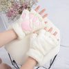 A pair of white plush cat claw mittens being held, with a pink flower arrangement in the background.
