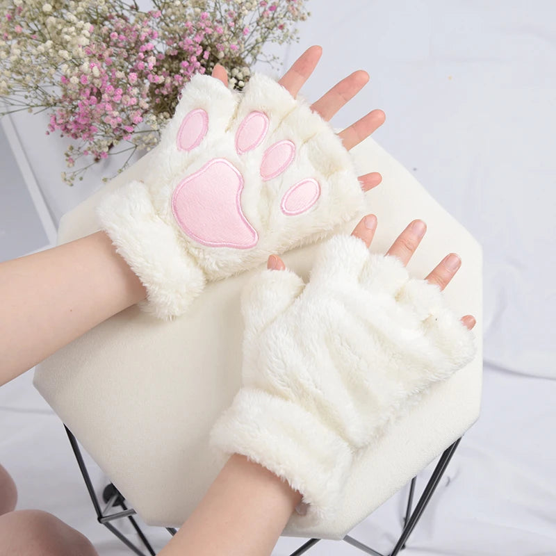 A pair of white plush cat claw mittens being held, with a pink flower arrangement in the background.