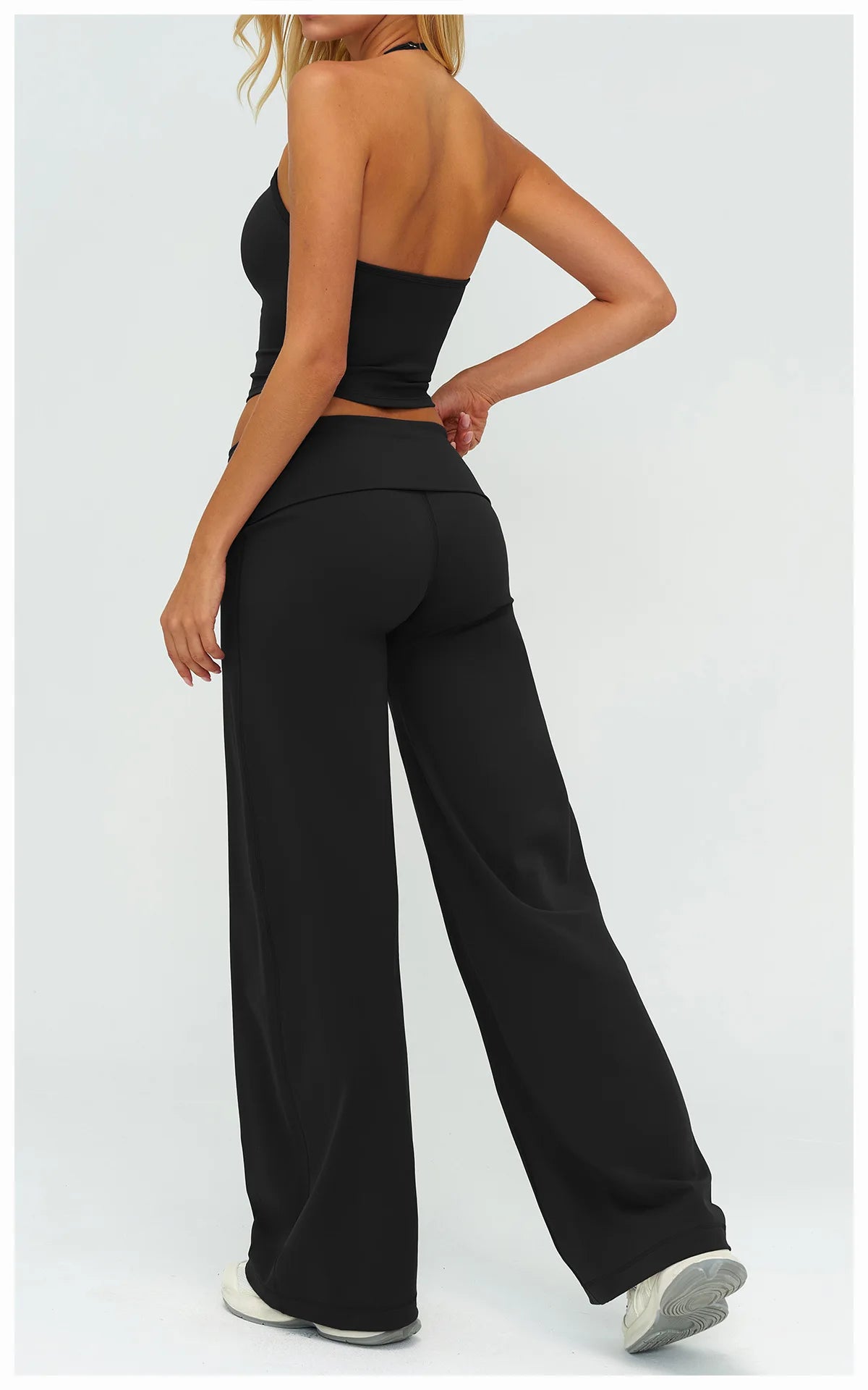 A woman models black flared high-waist yoga pants with a fitted crop top, shown from the back.