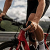 A person is riding a red bicycle while holding a black fitness tracker on the handlebars.