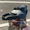 A black insulated sports water bottle with a clear cap is held by a hand against a gray outdoor background.