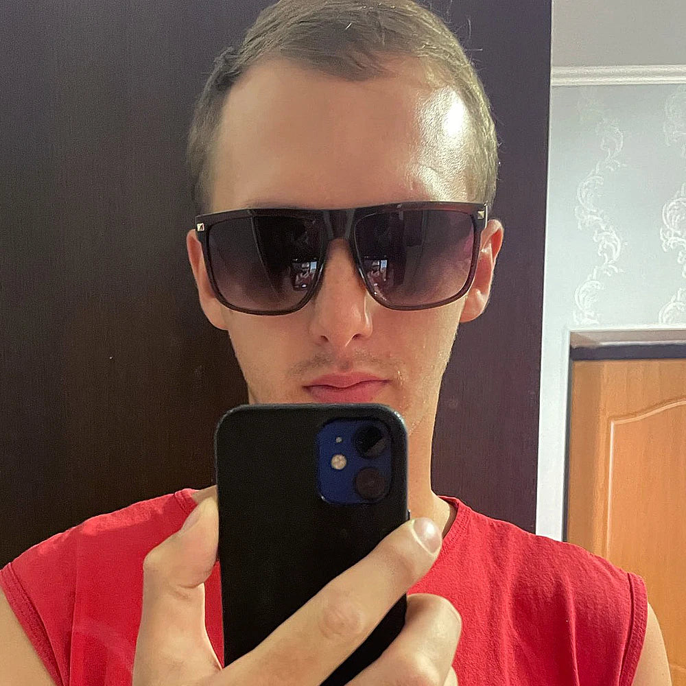 Ein Mann mit schwarzen, quadratischen Sonnenbrillen hält ein Smartphone.