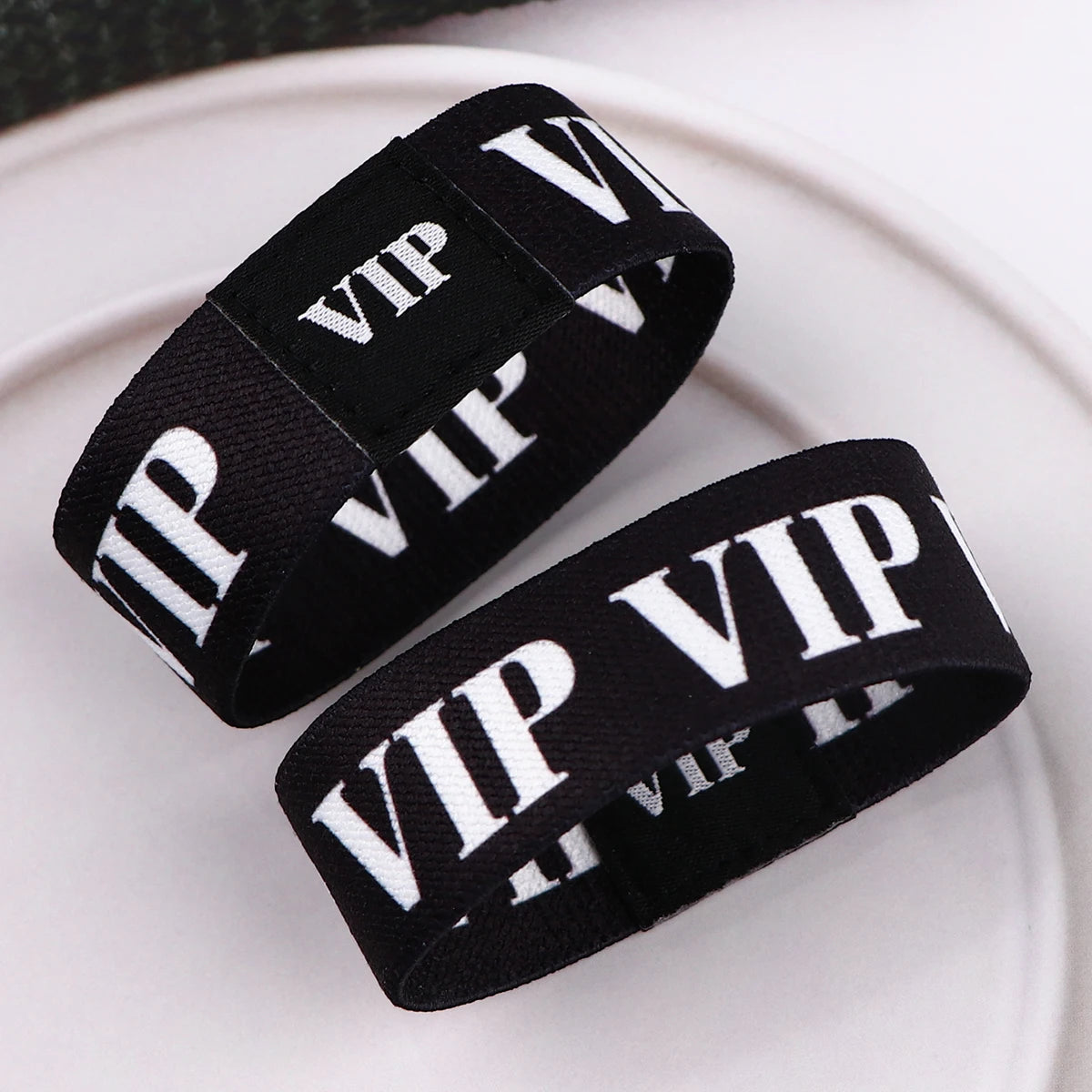 Schwarze Acryl-Elastik-Armbänder mit weißer VIP-Beschriftung auf einer weißen Platte.