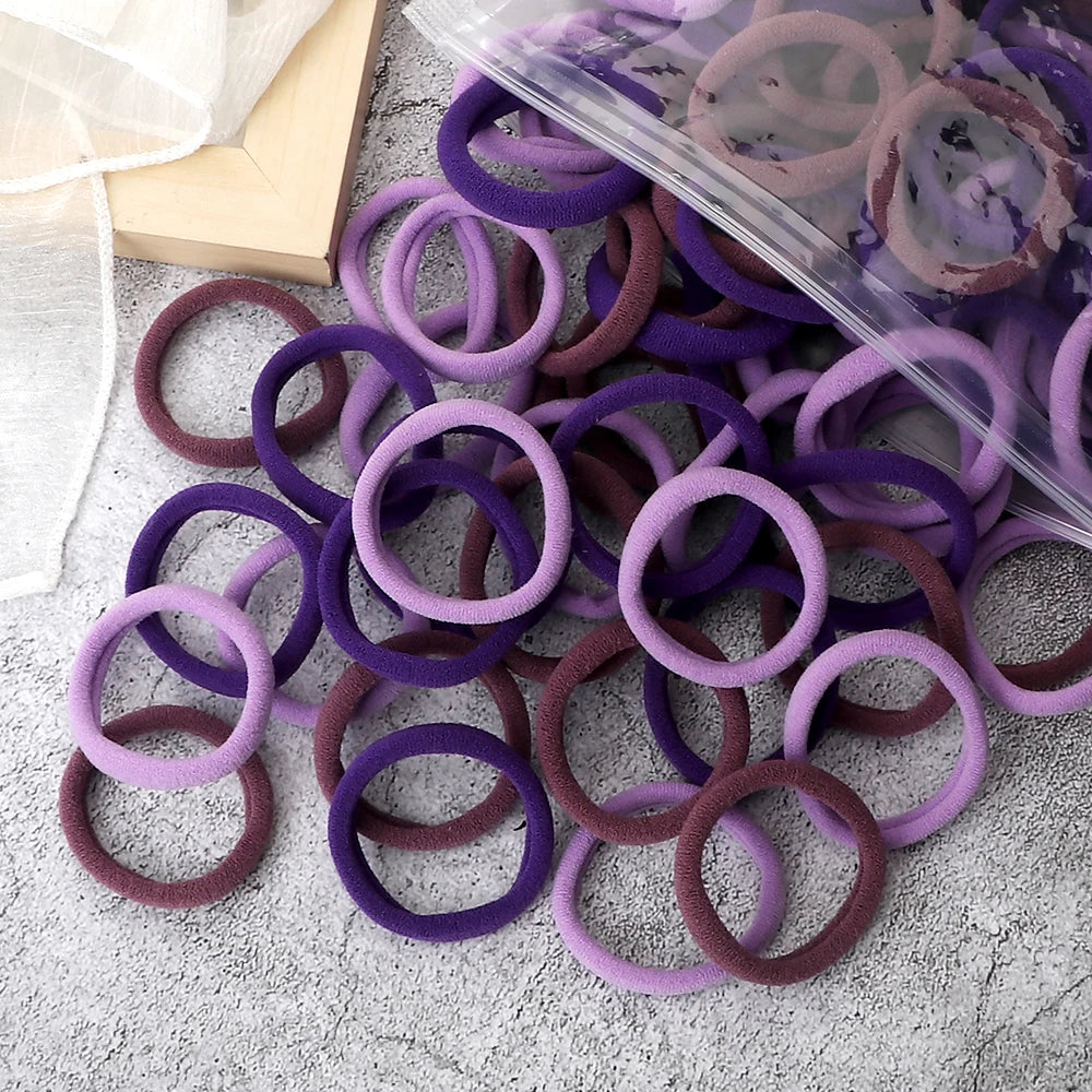 A pile of 50 mixed color elastic hair bands in purple and mauve shades, some packaged in clear plastic.