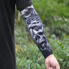 A person wearing a black shirt displays an arm covered in black and white skull tattoos on the sleeve.