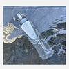 A clear silicone water bottle is submerged in dark water, showing its shape and texture.