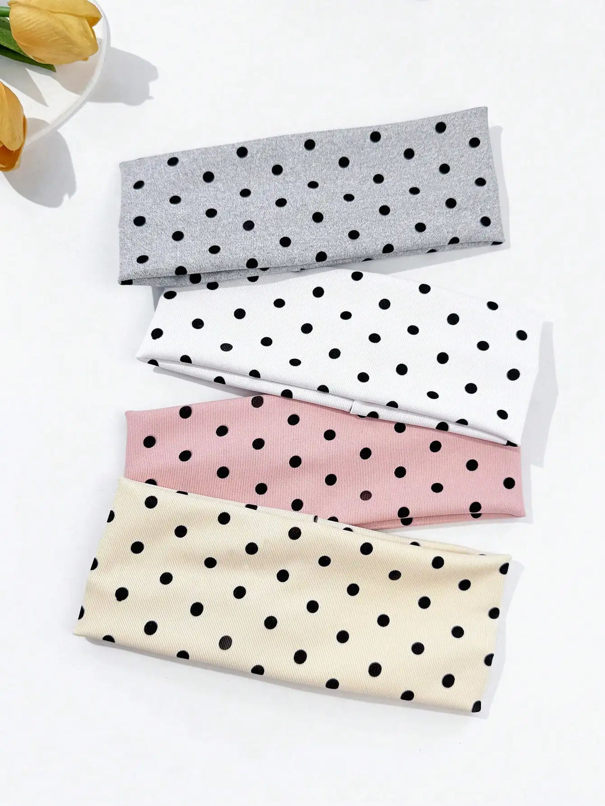 A set of four polka dot elastic hair bands in gray, white, pink, and beige are displayed on a white surface.