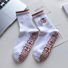 Paire de chaussettes de yoga blanches avec broderie de cœur marron et une petite feuille, posées sur une surface blanche.