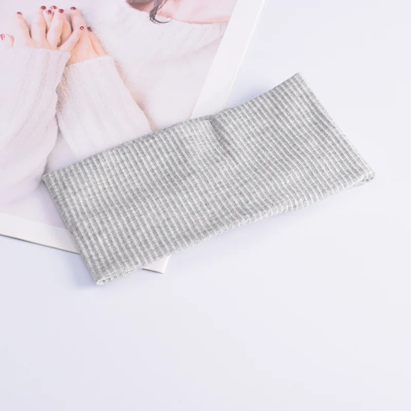A gray striped soft cotton knitted headband lying on a white surface next to a pink background.