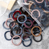 A pile of 50 mixed color elastic hair bands in various shades of gray, brown, and pink, with some packaged in clear plastic.