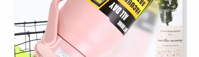 A pink insulated stainless steel water bottle with a yellow label is shown next to a potted plant.