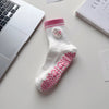 Chaussettes de yoga blanches avec broderie de cœur rose posées sur une surface blanche à côté d'un ordinateur portable et d'u