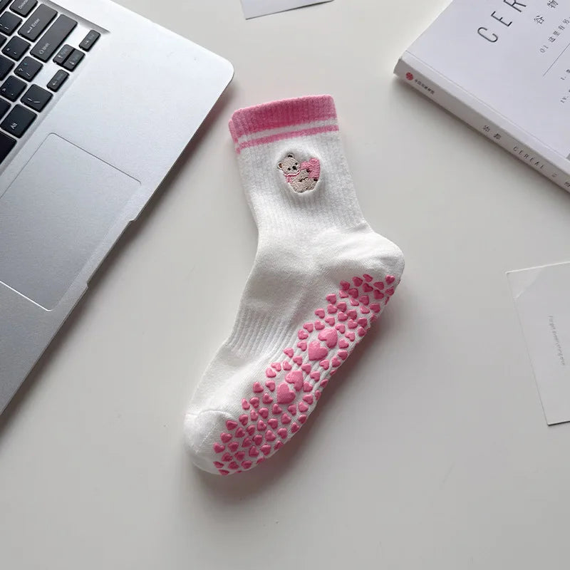 Chaussettes de yoga blanches avec broderie de cœur rose posées sur une surface blanche à côté d'un ordinateur portable et d'u