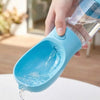 A hand is pouring water from a blue portable pet water and food dispenser into a white surface.