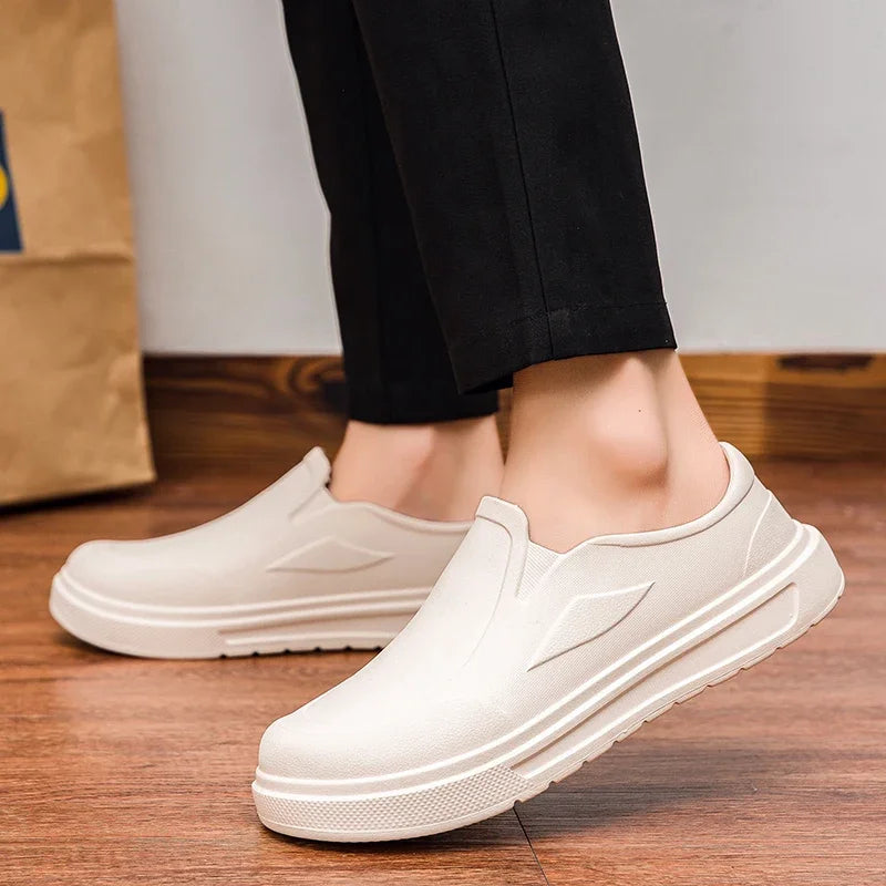 A pair of beige men's anti-slip oil-resistant kitchen clogs shown on a wooden floor.