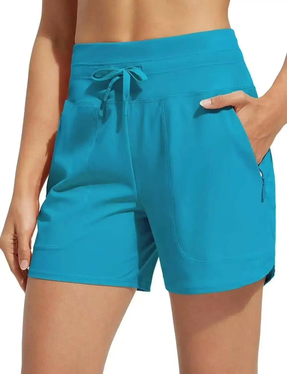 A woman is holding up a pair of teal high-waisted quick-dry athletic shorts.