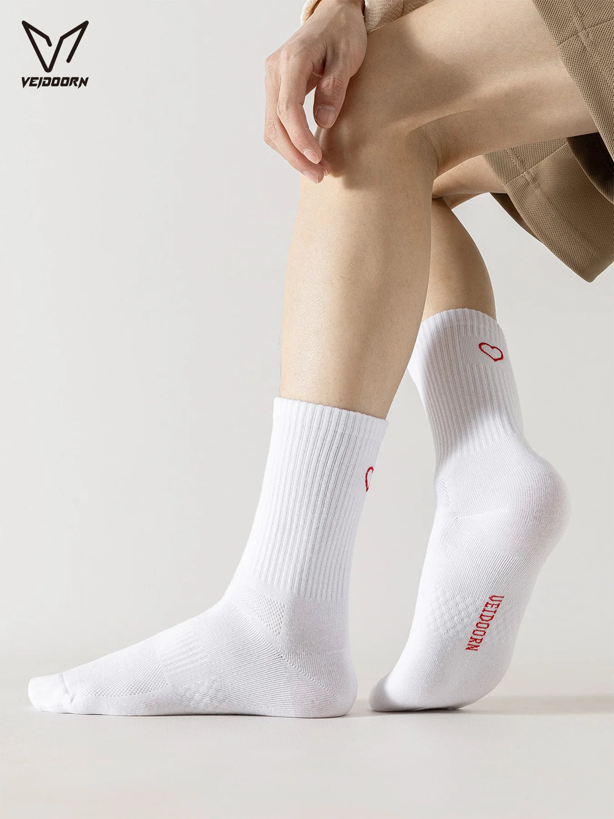 A close-up of white crew socks with a red heart detail worn on a person's leg.
