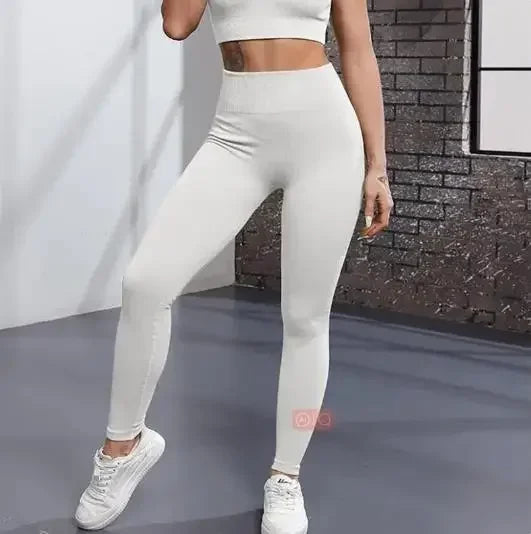 Une femme portant des leggings de yoga tricotés unis blancs et un haut court devant un mur de briques.