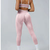 A woman models high-waist pink yoga leggings and a matching sports bra top in a studio setting.