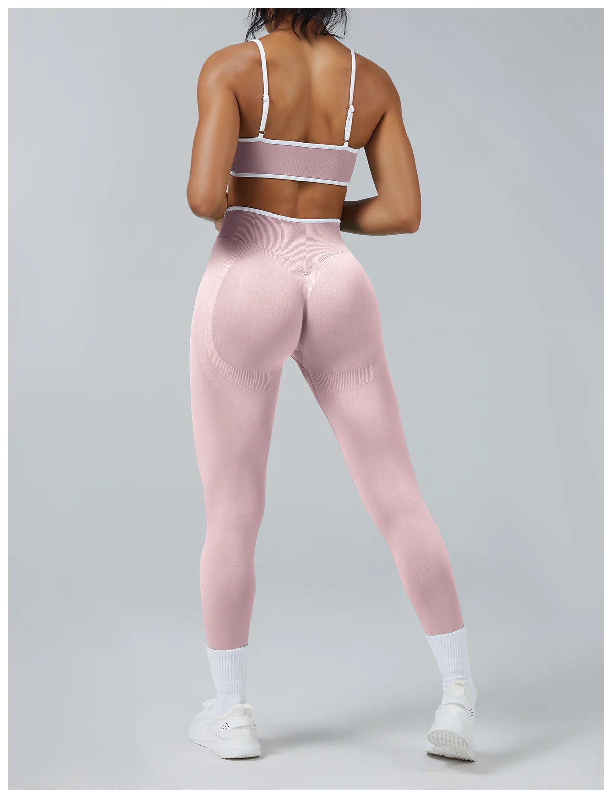 A woman models high-waist pink yoga leggings and a matching sports bra top in a studio setting.