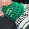 A hand is holding a bright green knitted sock with white embroidery that reads What's snack or snack today on a leopard print