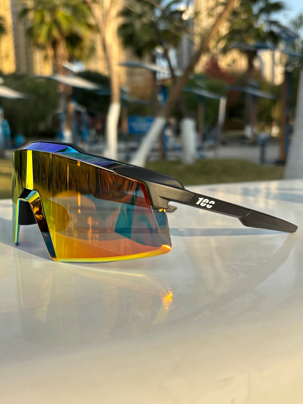 A pair of orange-tinted sports sunglasses resting on a white surface outdoors.