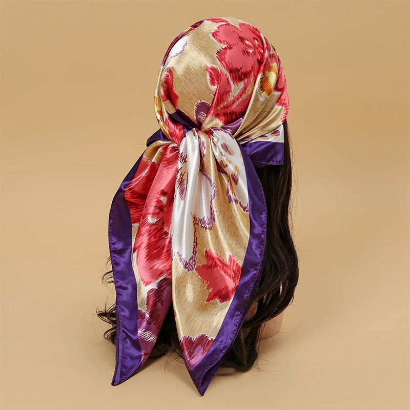 A vibrant pink and gold floral satin square scarf tied around a dark hair, featuring purple trim.