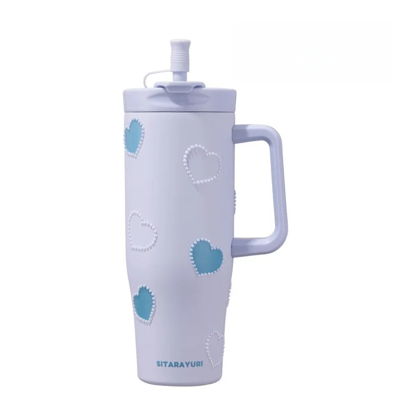 A white insulated thermos mug with a light purple hue decorated with heart-shaped pearl inlays.