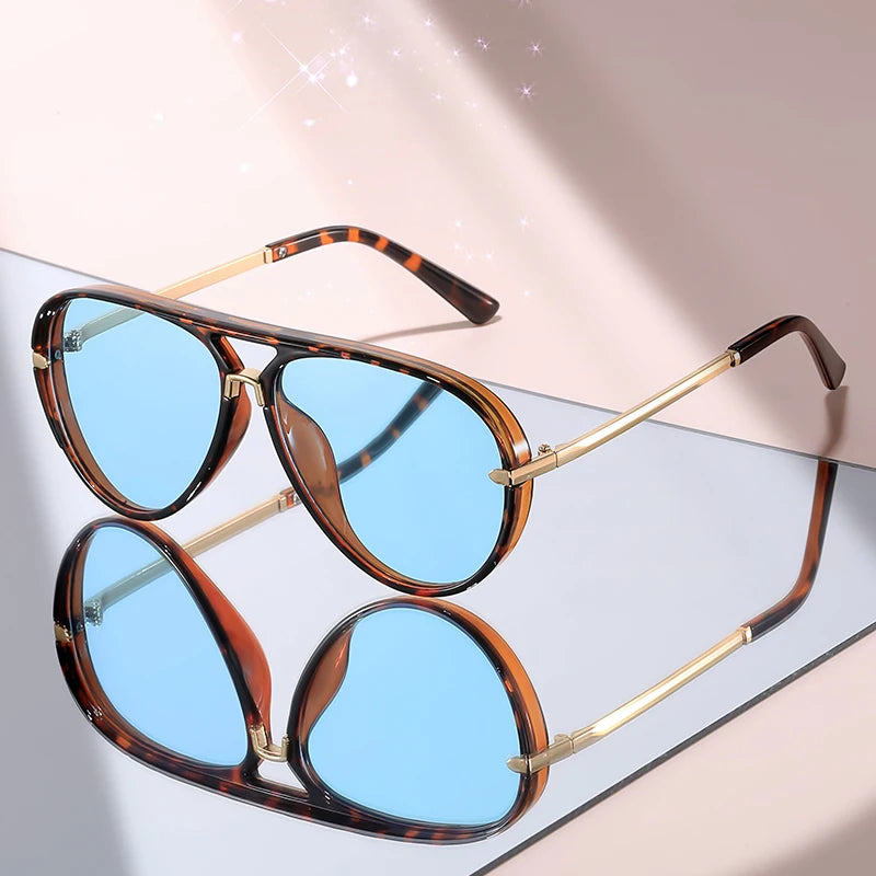 Brown tortoiseshell framed aviator sunglasses with gold accents resting on a light surface.
