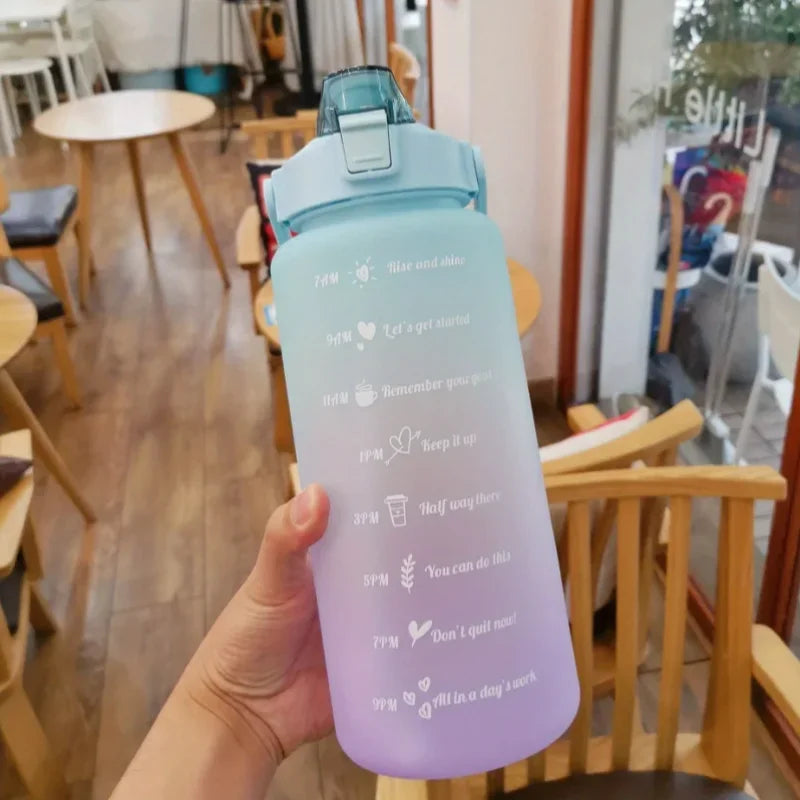 Una mano sostiene un set de botellas deportivas para agua con gradiente púrpura claro y pajita en un entorno interior.