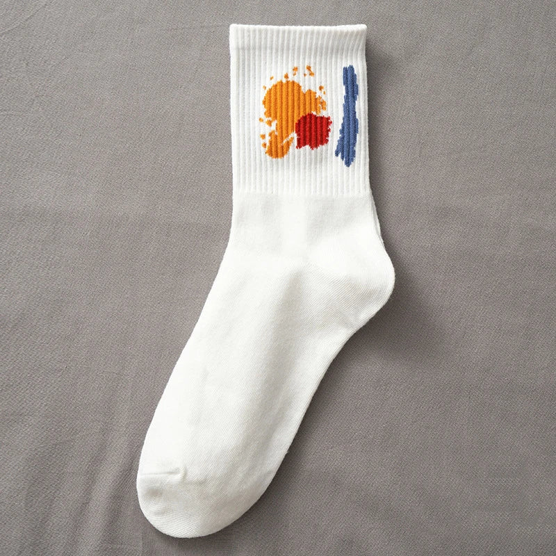 A white sock with orange and blue paint splatters on the top, displayed against a gray background.