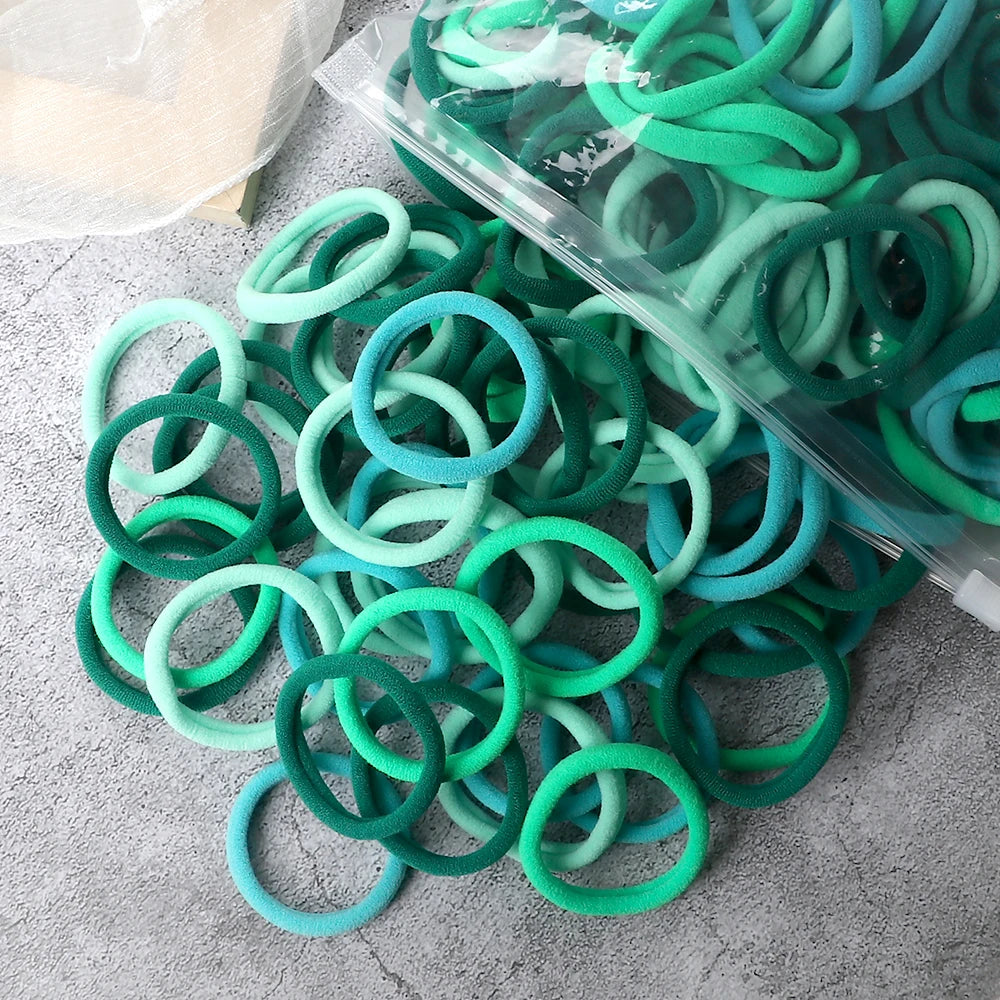 A pile of 50 pieces of mixed color elastic hair bands in shades of green and blue.