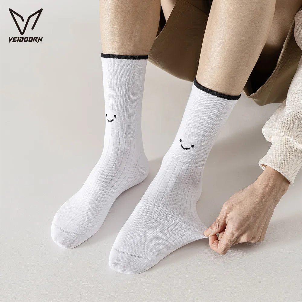 A pair of white crew socks with a smiling face design being held by a person's hand.