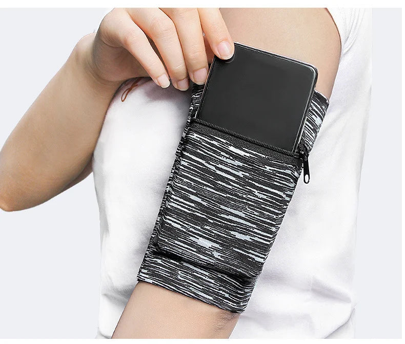 A hand is holding a black zippered wrist bag with a black phone inside, featuring a black and white striped pattern.