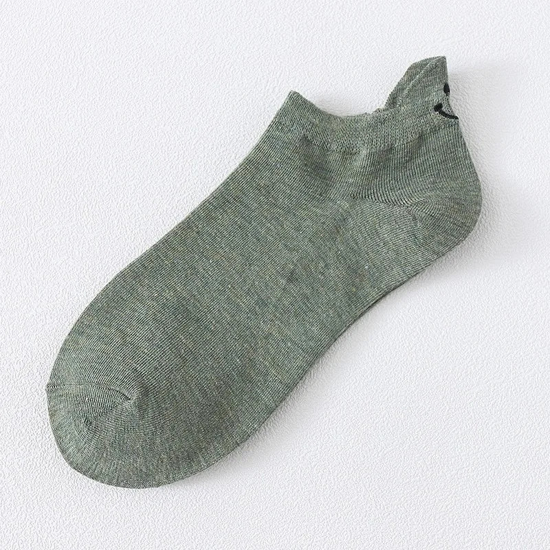 Un par de calcetines de tobillo verde oliva con una pequeña cara sonriente negra bordada en la punta.