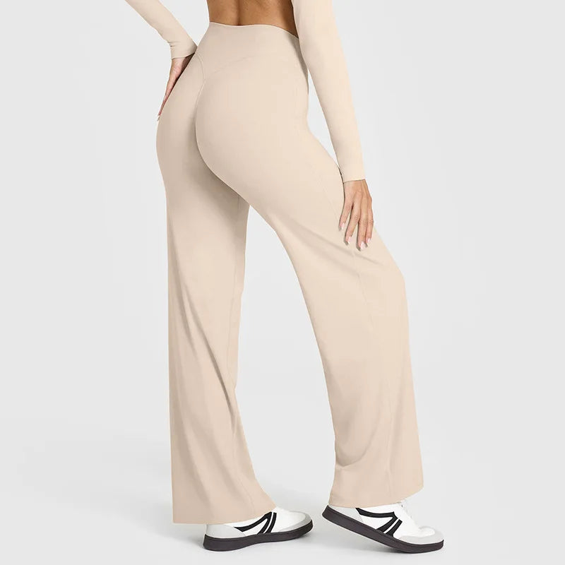 A model wearing beige high-waist yoga pants and a long-sleeved top, standing in a neutral pose.