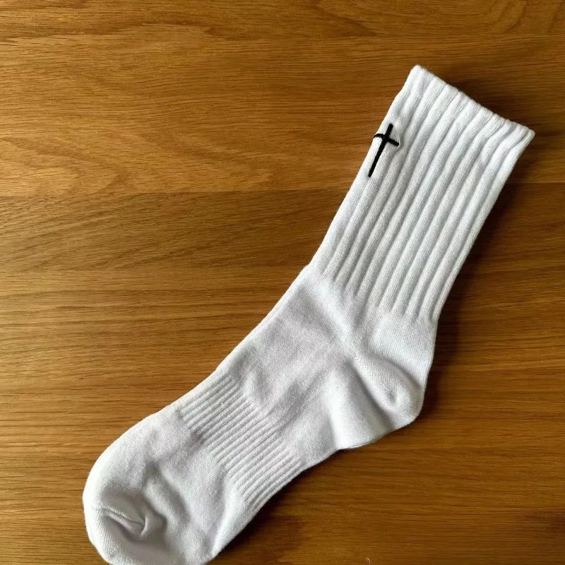 A white mid-length cotton sock with a cross design lying on a wooden surface.