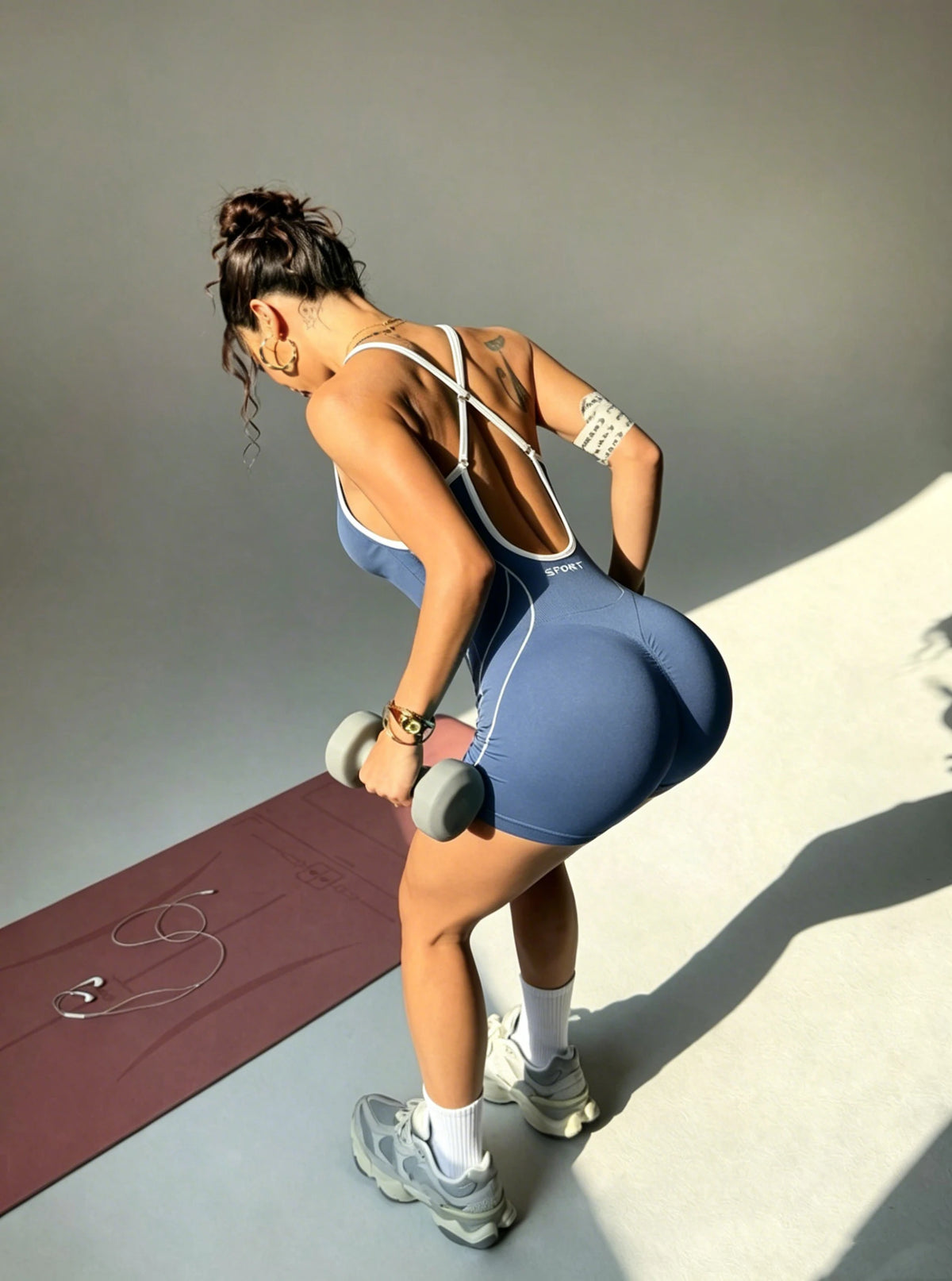 Eine Frau in einem blauen, nahtlosen Yoga-Overall führt eine Fitnesspose in einem Studio aus.