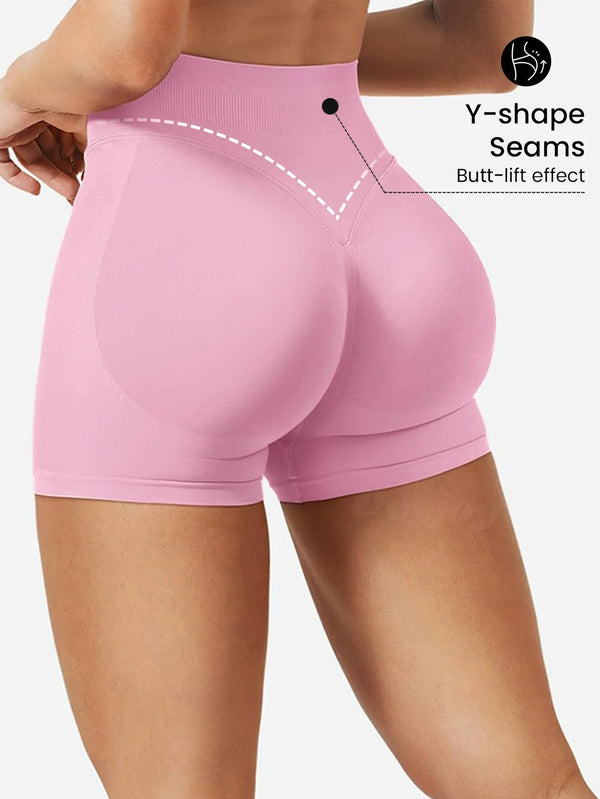 A model wears pink high-waisted knit fitness shorts highlighting the Y-shape seams and butt-lift effect.