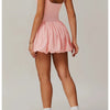 Modelin trägt ein pinkes Performance-Tenniskleid mit plissierter Rock und weißen Socken und grauen Turnschuhen.