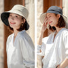 A woman wearing a wide brim bucket hat and a white shirt outdoors.