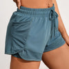 A close-up of a teal athletic pair of shorts with mesh pockets and an adjustable drawstring waist.