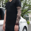 Une personne portant un t-shirt noir avec une longue manche de tatouage foncé sur son bras, debout à côté d'une voiture blanc