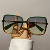 A hand holds a pair of retro two-tone gradient sunglasses with green and amber lenses and dark frames.