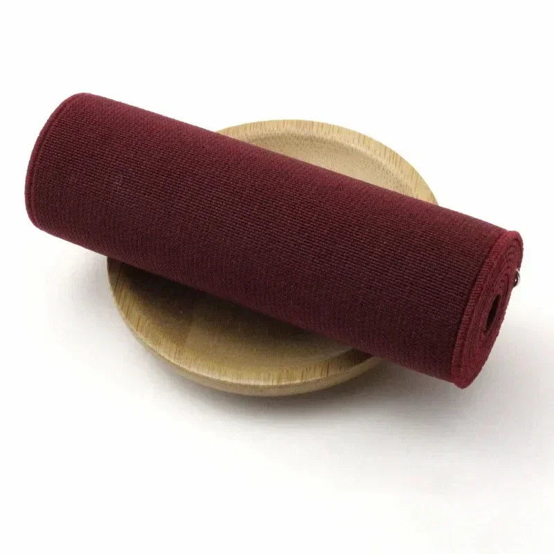 A roll of dark burgundy elastic band resting on a light wood plate.