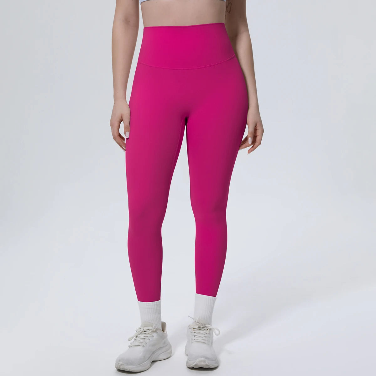 A model wearing bright magenta high-waisted quick-drying yoga and fitness leggings and white socks and athletic shoes.
