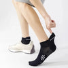 A close-up of a person wearing black breathable running socks with white accents and a light-colored athletic shoe.