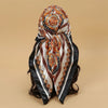 An elegant satin square scarf featuring intricate floral patterns in orange, gold, and white on a black background.
